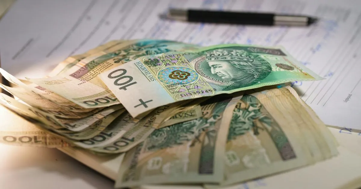 Banknoty stuzłotowe leżące na dokumentach obok długopisu
